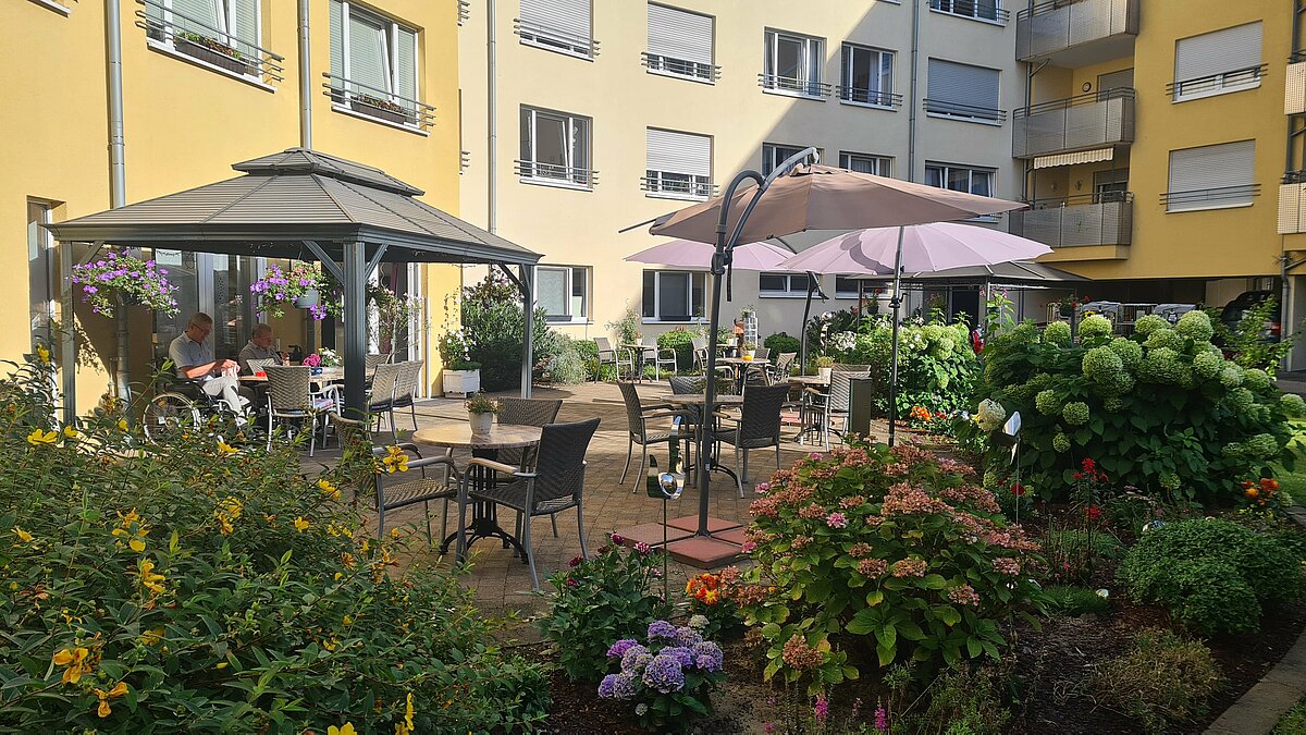 Garten mit vielenBlumen, auf der Terrasse große Sonnenschirme und Pavillon als Schattenspender